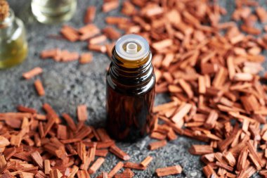 A dropper bottle of aromatherapy essential oil with red sandalwood in the background