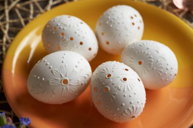 Handmade white Easter egg decorated with wax with drilled holes on an orange plate