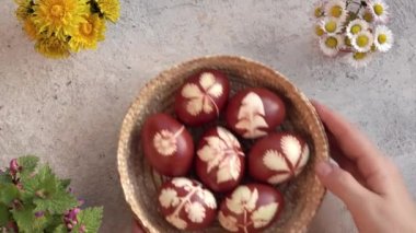 Bir kadının elleri masaya soğan kabuklarıyla boyanmış el yapımı Paskalya yumurtalarını hasır sepete koyuyor.