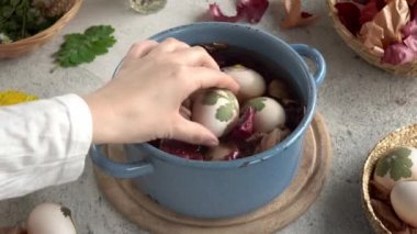 Üzerine taze yapraklar yapıştırılmış Paskalya yumurtalarını boyamak için soğan kabuklarıyla dolu bir tencereye koyuyorlar.