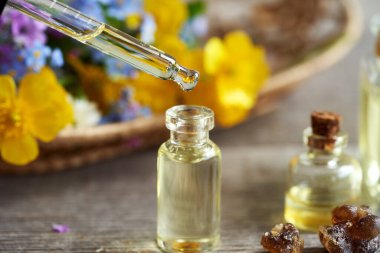 Cam bir şişeye aromaterapi yağı döküyorum. Arka planda tütsü reçinesi ve bahar çiçekleri var.