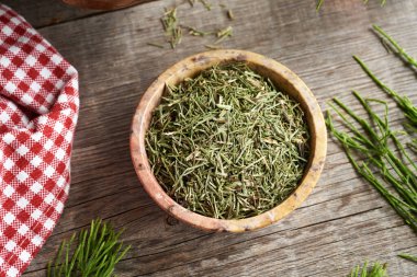 Bir kase kurutulmuş at kuyruğu otu ve masada taze Equisetum bitkisi.