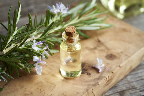 Прозрачная бутылка ароматерапевтического эфирного масла со свежими цветущими розмариновыми ветками