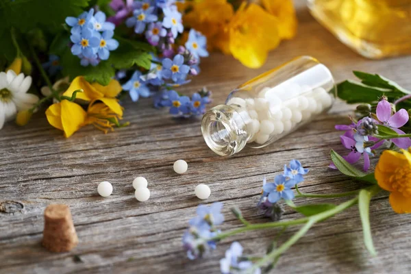 stock image A glass bottle with spilled homeopathic globules, with spring herbs and flowers