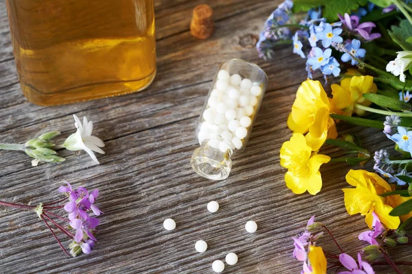 stock image A bottle of homeopathic pills or globules with colorful flowers and herbs in spring on a wooden table