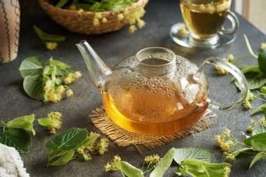 Bitki çaydanlığında taze ıhlamur ya da Tilia çiçek ve yapraklarıyla bir masa.