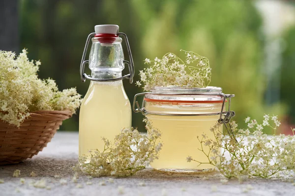 Bottles of homemade elder flower syrup with fresh blossoms on a table outdoors
