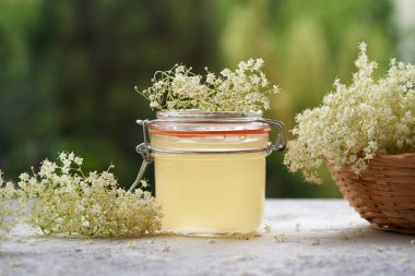Bir kavanoz ev yapımı siyah yaşlı çiçek şurubu açık bir masada.