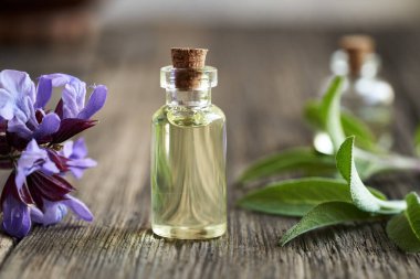 Masanın üzerinde mor adaçayı çiçekleri olan gerekli yağ şişesi.