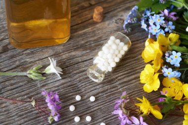 Tentürü, taze bahar çiçekleri ve bitkileri olan bir şişe homeopatik hap.