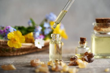 Tütsü kristalleri ve arka planda renkli bahar çiçekleri olan cam bir şişeye gerekli yağı dökmek.