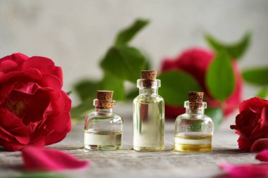 Üç şişe aromaterapi esaslı yağ ve ahşap masa üzerinde kırmızı gül çiçekleri.