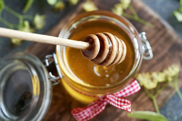 Een Honingdipper Boven Een Glazen Pot Met Verse Lindebloemen Achtergrond — Stockfoto