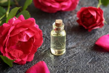 Koyu arkaplanda kırmızı gül çiçekleri olan şeffaf bir aromaterapi şişesi.