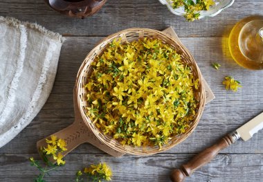 Taze St. John otları ya da yazın toplanan Hypericum çiçekleri bir sepetin içinde, masanın üstünde.