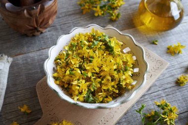 Aziz John otları ya da Hypericum çiçekleri yazın bir kasede toplanır ve arka planda bir şişe yağ bulunur.