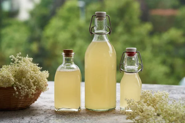 stock image Three bottles of elderberry flower syrup with fresh blossoms on a table outdoors