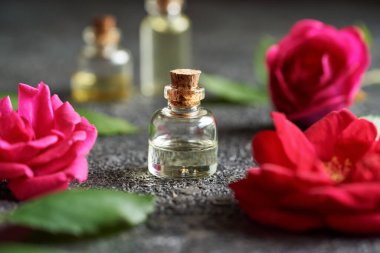 Siyah arka planda kırmızı gül çiçekleri olan şeffaf bir yağ şişesi.