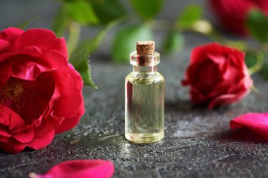 Siyah arka planda kırmızı gül çiçekleri olan şeffaf bir yağ şişesi.