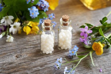 Cam şişelerde beyaz homeopatik haplar ve taze renkli bahar çiçekleri.
