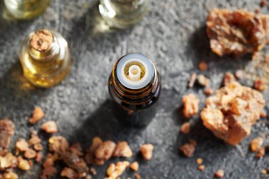 Gri arkaplanda reçine olan koyu bir yağ şişesi.