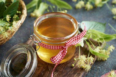 Bahar aylarında toplanan ıhlamur çiçekleri ve yapraklarla dolu cam bir kavanozda bal