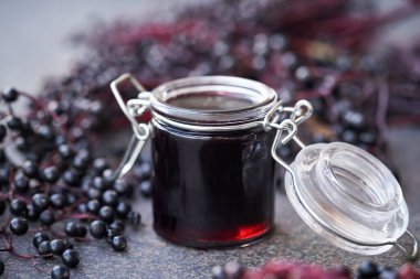 Arka planda taze mürver içeren kavanozda ev yapımı siyah yaşlılar şurubu.