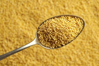 Sarı arka planda bir kaşıkta soyulmuş darı, üst manzara 