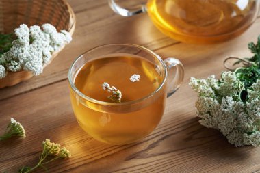 Masanın üzerinde taze Achillea Milleyum çiçekleri olan şeffaf bir fincan kiremit çayı.