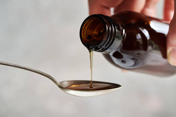 Pouring healthy herbal syrup from a glass bottle onto a metal spoon