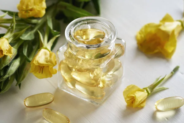 Evening primrose oil gel capsules with Oenothera biennis flowers on a white table
