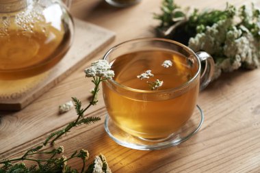 Cam bir fincanda bitkisel çay ve masada taze kiremit çiçekleri.