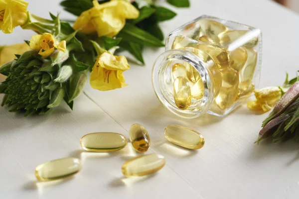 Gel capsules of evening primrose oil spilled from a glass bottle on a white table. Nutritional supplement.