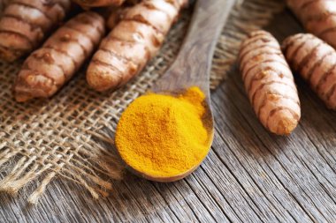 Tahta kaşıkta Curcuma tozu. Arka planda taze zerdeçal kökü var.