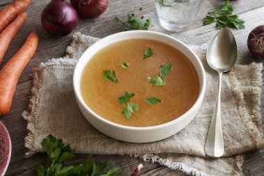 Tavuk çorbası ya da kemik suyu beyaz bir kâse içinde bir kaşık ve taze sebze.