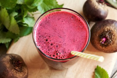 Cam bardakta kırmızı pancar suyu, taze pancar kökü ve arka planda Melissa.