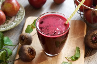 Kırmızı pancar suyu bardakta, taze elmalar, pancar kökü ve Melissa arka planda.