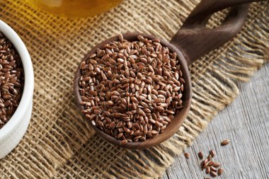 Ahşap kaşıkta keten tohumu, arka planda keten tohumu yağı şişesi.