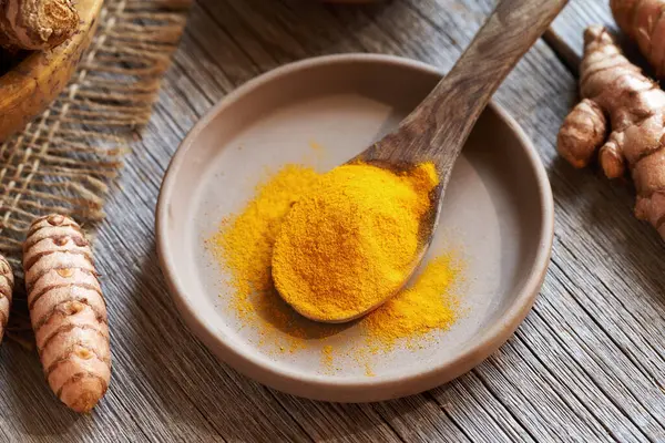 stock image Curcuma powder on a wooden spoon with fresh turmeric root