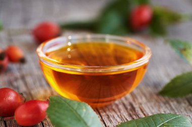 A bowl of rose hip seed oil with fresh rosehips on a table