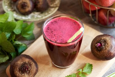 Arka planda taze elmalar olan bir fincan kırmızı pancar suyu.