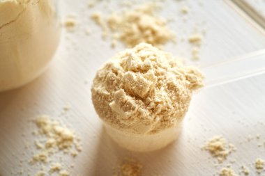 Beyaz bir masada plastik bir ölçü kabında beyaz protein tozu.