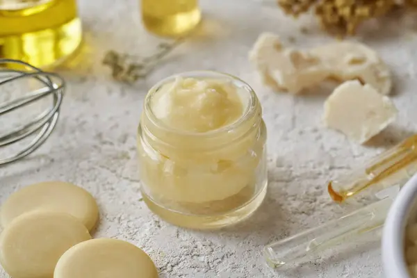 Homemade cosmetic cream with cocoa butter, essential oils and shea butter in the background
