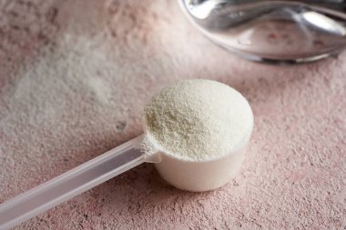 Pembe arka planda plastik bir kaşık içindeki kolajen tozu