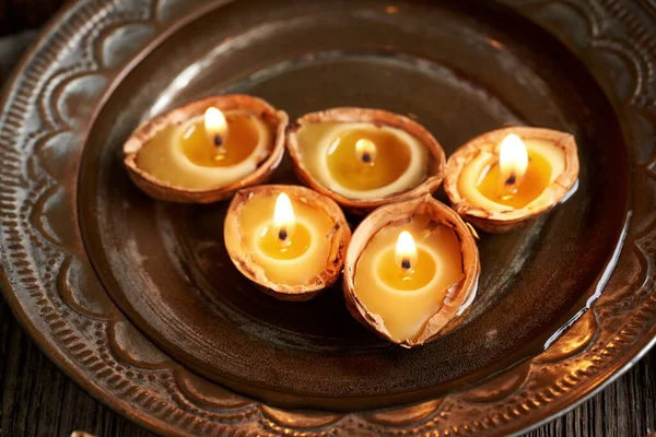 Five Christmas candles made of bees wax and nut shells floating in a bowl of water, close up