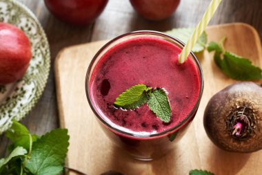 Kırmızı pancar suyu bardakta, taze elmalar, pancar kökü ve Melissa arka planda.