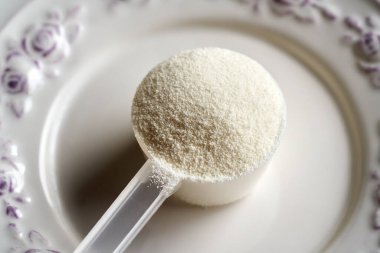 Collagen powder in a plastic measuring scoop on a white plate clipart