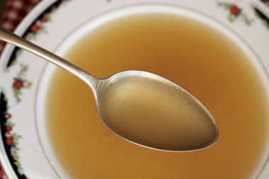 Çorba kasesinin üstündeki metal kaşıkta tavuk kemiği çorbası.