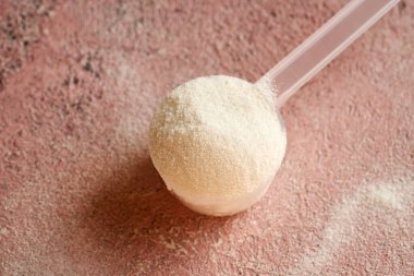 Collagen powder in a plastic measuring spoon on pink background clipart