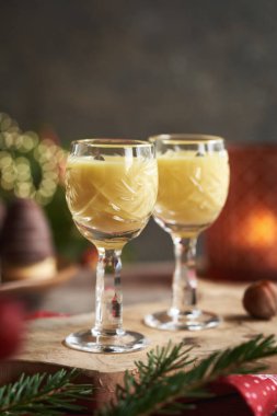 Arka planda Noel kurabiyeleri ve ağaç dalları olan iki bardak eggnog.